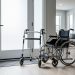 Mobility aids including a cane, rolling walker, and wheelchair placed near an accessible doorway and ramp threshold in a bright home.